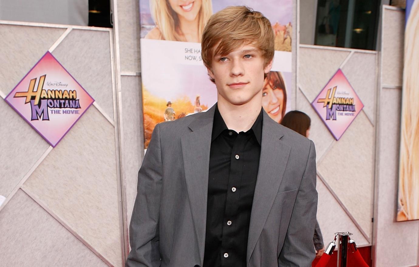 Lucas Till in a gray suit on the red carpet