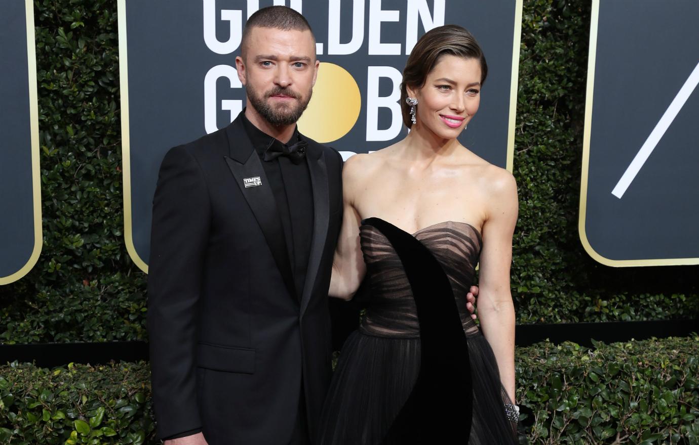 Justin Timberlake, in a black suit and black top, stands next to Jessica Biel in a black, lacy dress on the red carpet.