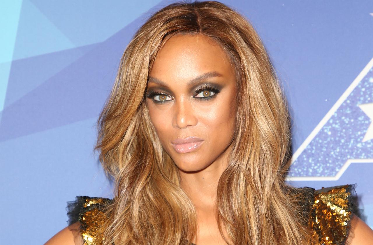 Tyra Banks wears a bronze sequined butterfly sleeve dress, smokey eyes, and long wavy blonde hair at the 2017 America’s Got Talent taping.