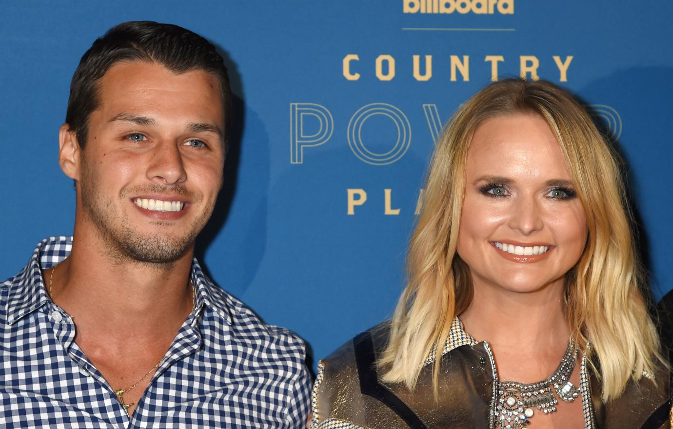 A smiling Brendan McLoughlin, in a blue check shirt, stands next to a smiling Miranda Lambert in a beige patterned jacket and white top.