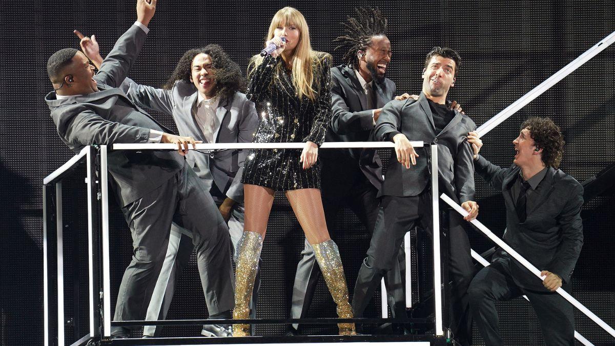 A photo of Taylor Swift on stage at the Eras Tour flanked by backup dancers