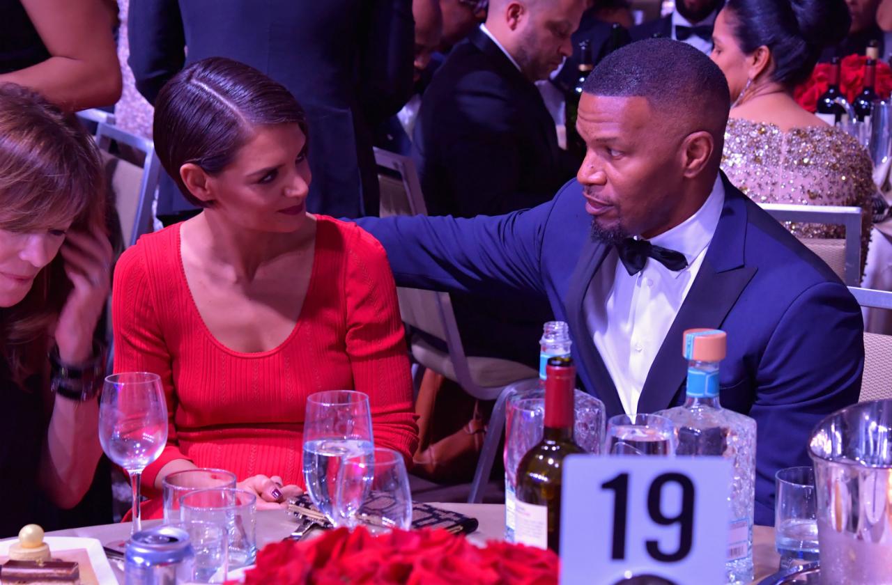 katie holmes in a red dress and jamie foxx in a tuxedo sit at a table together