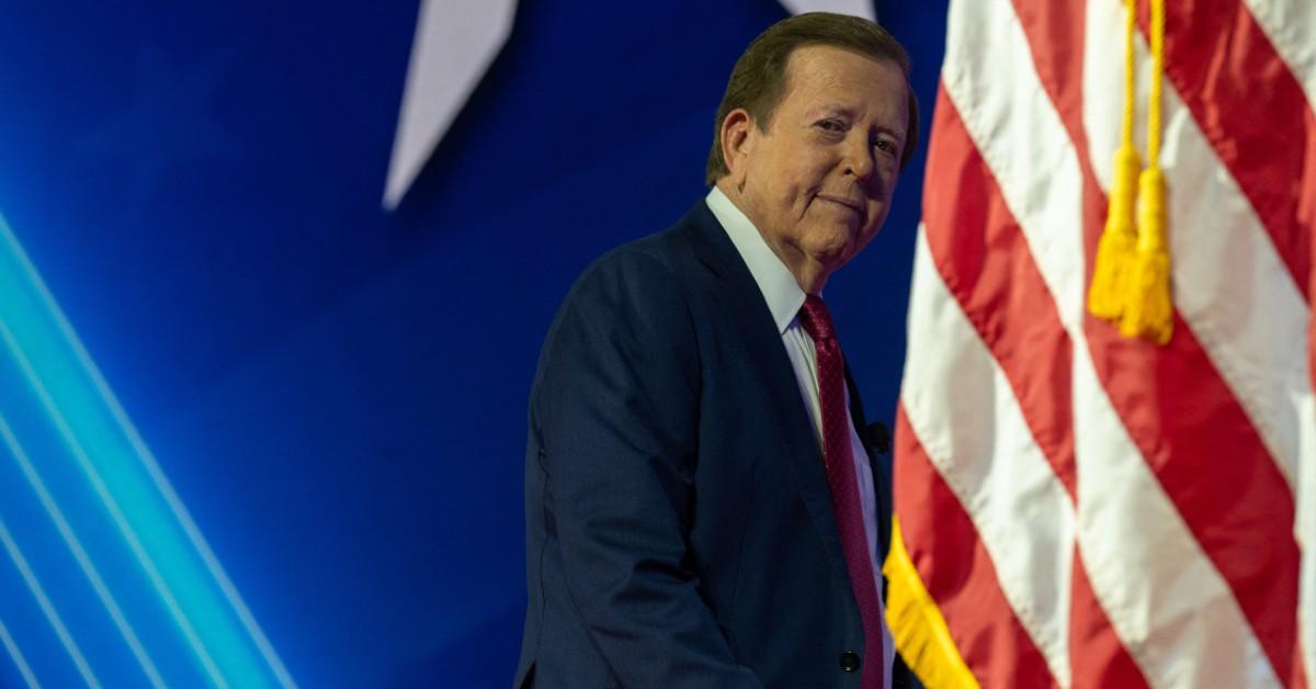 Photo of Lou Dobbs standing by American flag.