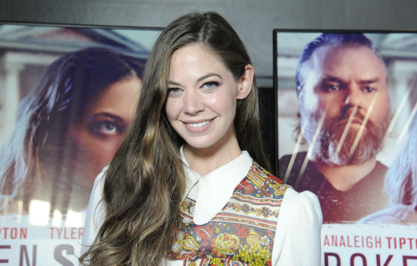 Analeigh Tipton, in a white dress with paisley trim, smiles on the red carpet.