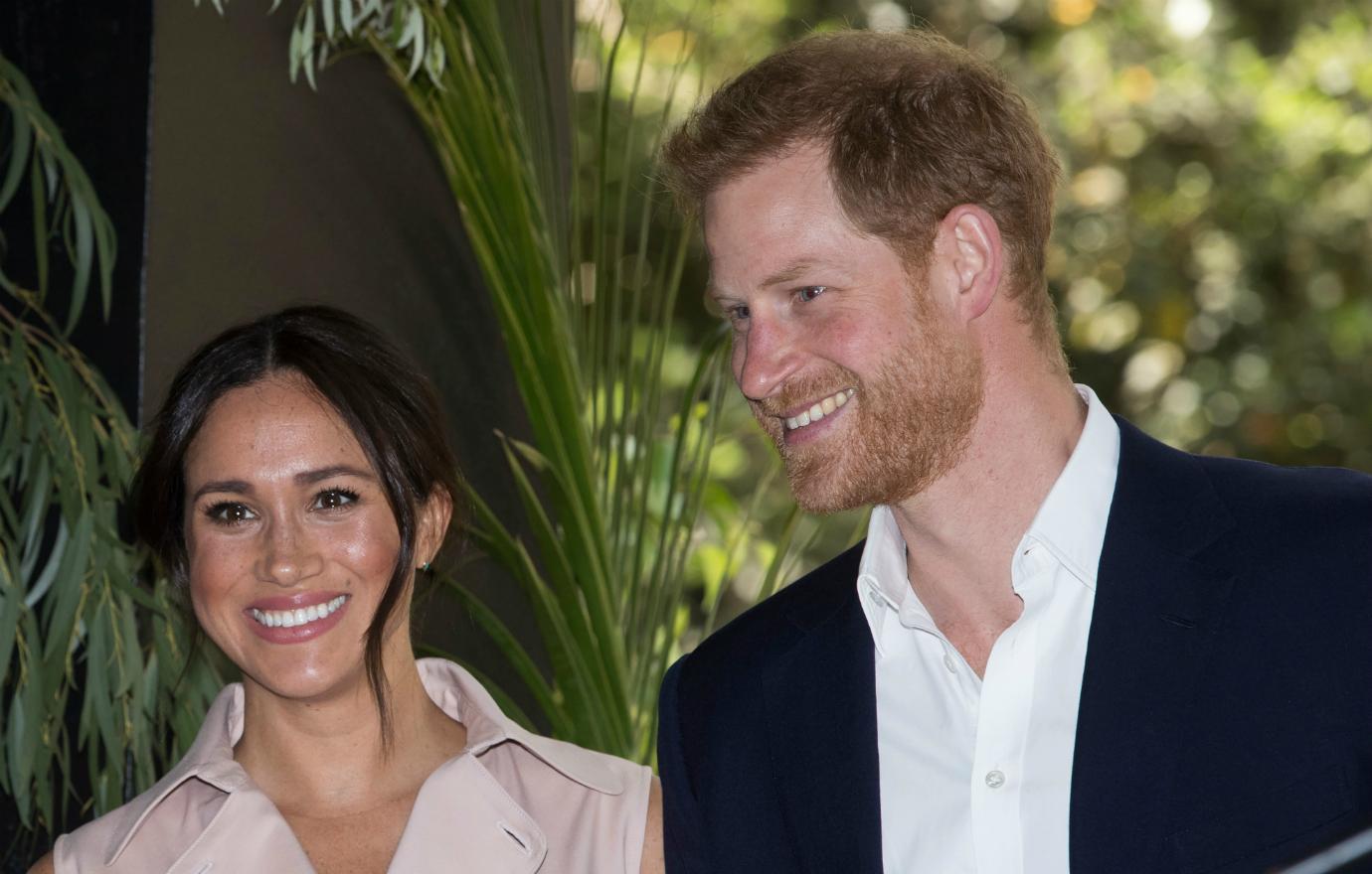 Prince Harry, in whiet shirt and black jacket, stands next to his wife.