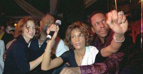 Whitney Houston, in black and clutching a mic, is flanked by Bobby Brown and Gloria Estefan.