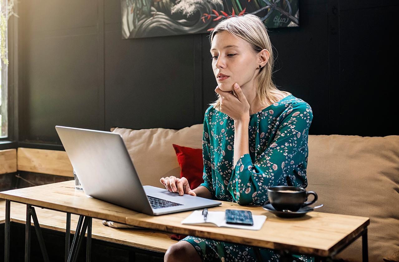 young woman with green dress sitting in café working on her laptop