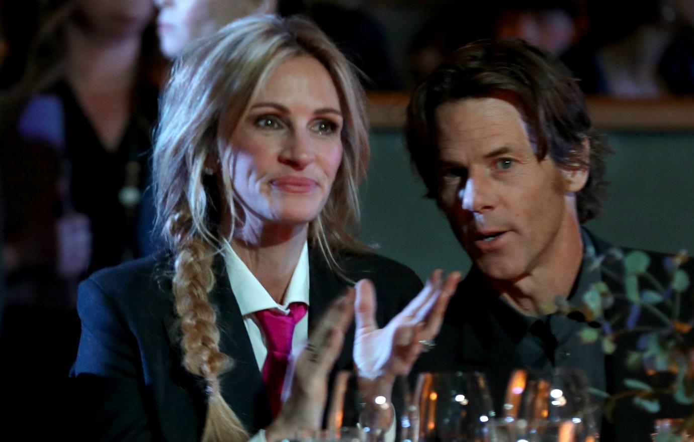 Juliet Roberts, in a black jacket, white shirt, and red tie, sits at a dinner table next to Danny Moder who wears black.