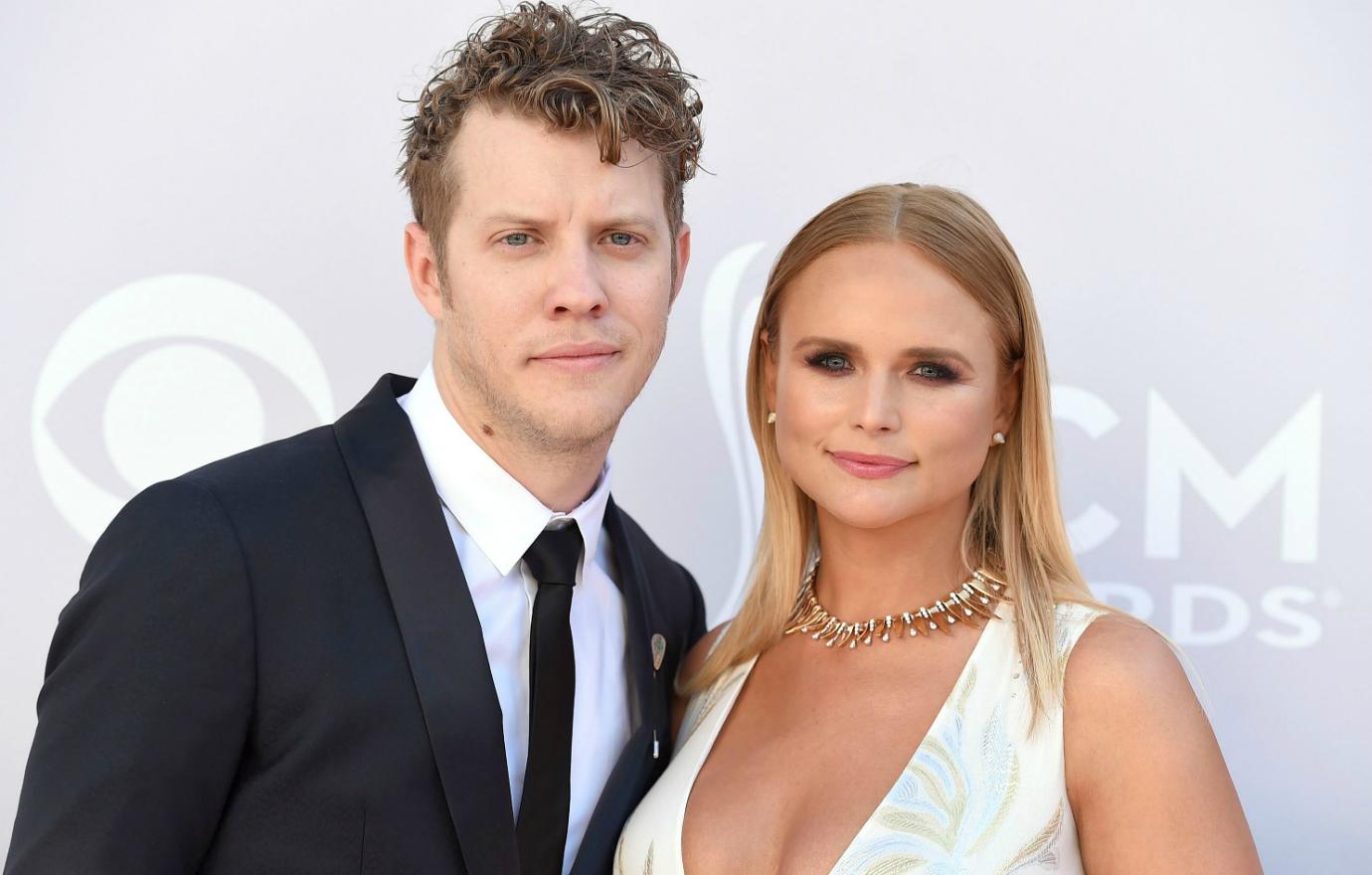 Anderson East, in black suit and white tie, stands next to Miranda Lambert who wears a low cut white dress.