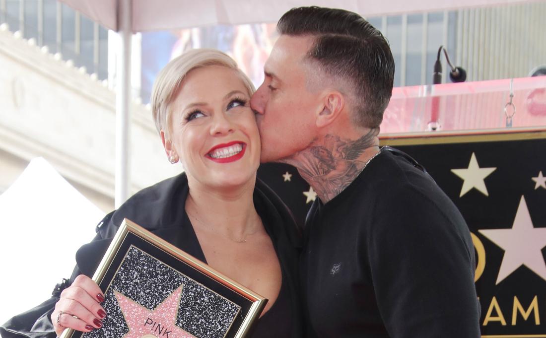 Pink, in a black and white dress, clutches a walk of fame picture and is being kissed by Carey Hart.