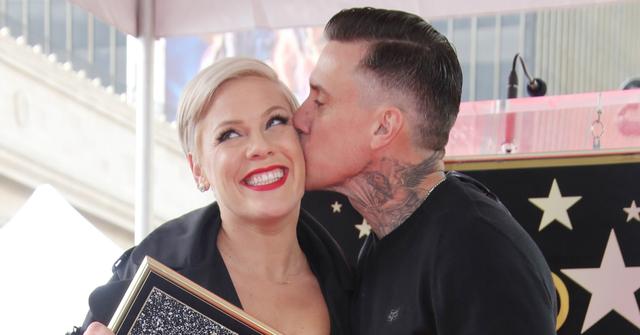 Pink, in a black and white dress, clutches a walk of fame picture and is being kissed by Carey Hart.