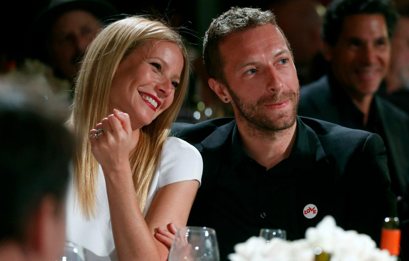 Chris Martin & Gwyneth Paltrow pose together at a dinner table.