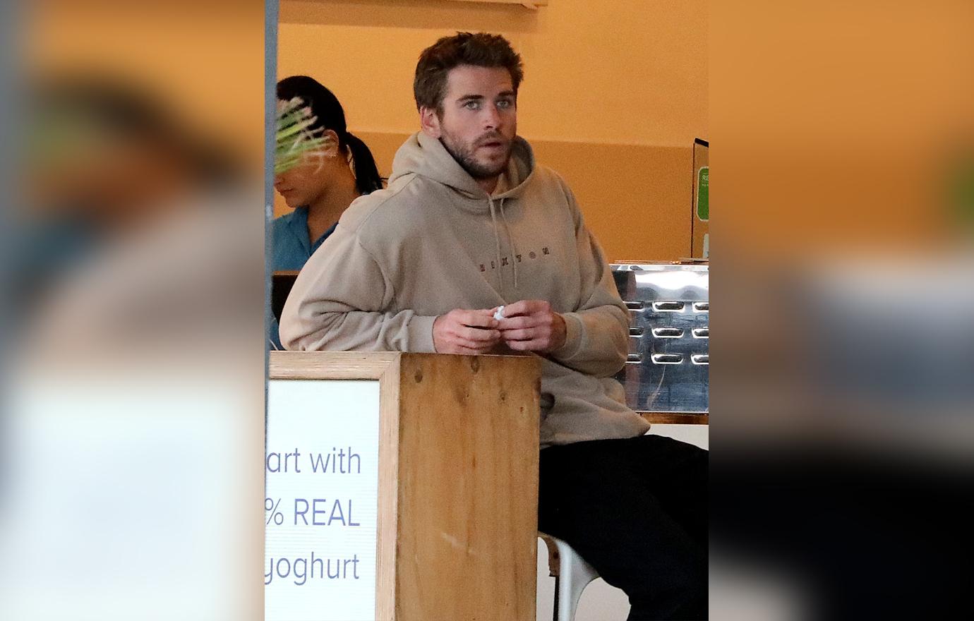 Liam Hemsworth Seen Sitting Down Inside Wearing a Beige Hoodie Looking Downtrodden