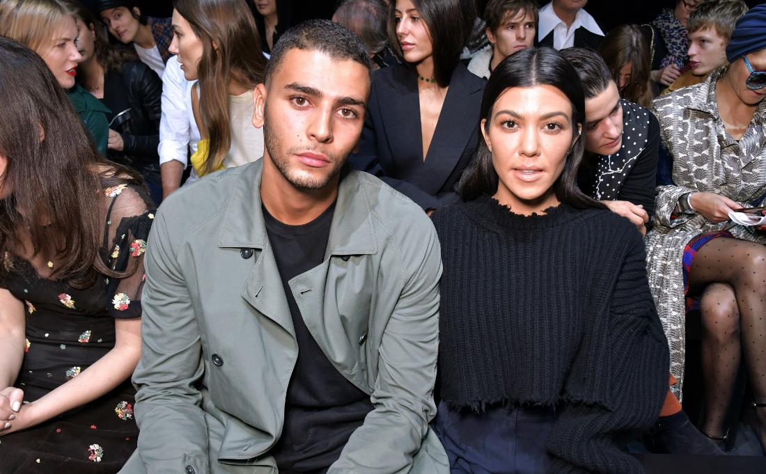 Kourtney Kardashian is all in black and sits next to Younes Bendjima who wears a grey jacket and black top.