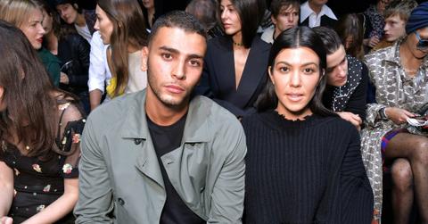 Kourtney Kardashian is all in black and sits next to Younes Bendjima who wears a grey jacket and black top.