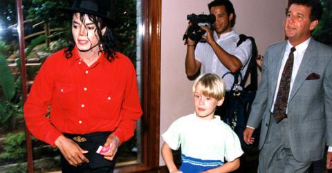 Michael Jackson in a red buttoned-down shirt with black pants posed with Macauley Culkin in a pair of shorts and a yellow and blue shirt.