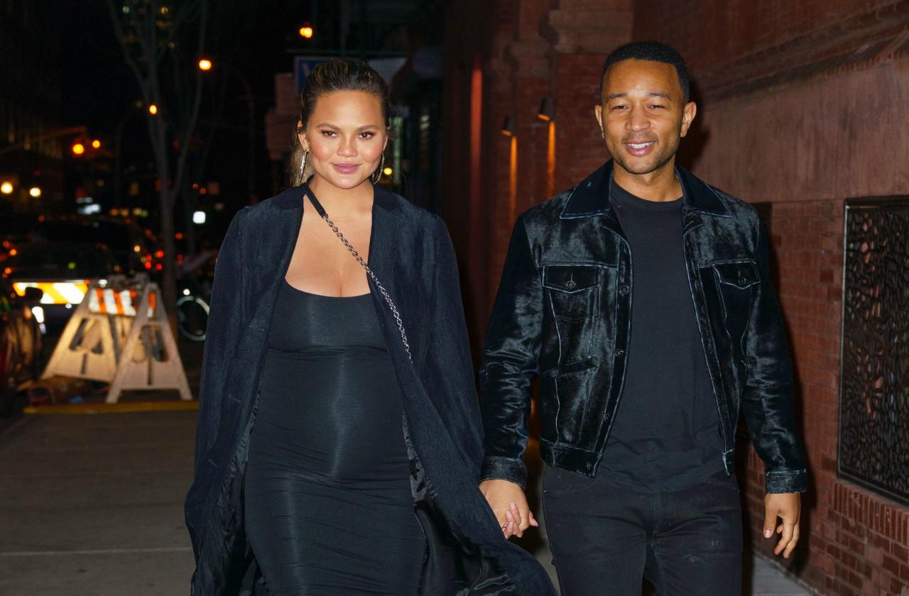 John Legend and Chrissy Teigen, both in black, hold hands and walk down a NYC street