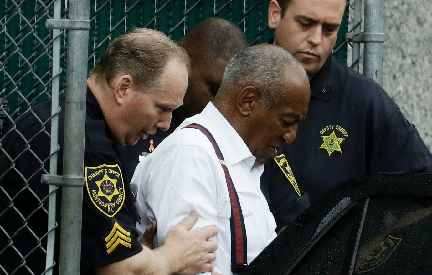 Bill Cosby, in a white shirt, is led into a car by police.