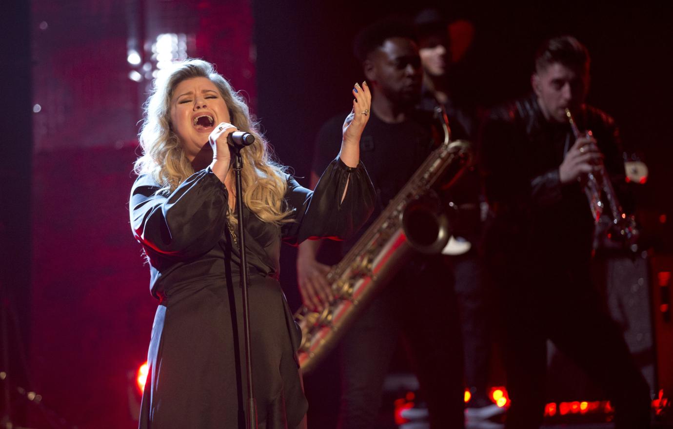 Kelly Clarkson in a black dress, singing with a band backing her