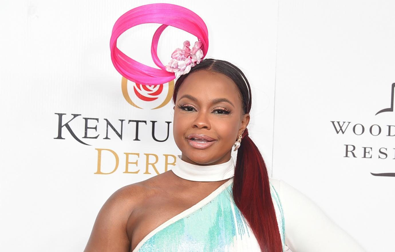 Phaedra Parks wears a choker, pink hat, and dress on a red carpet.