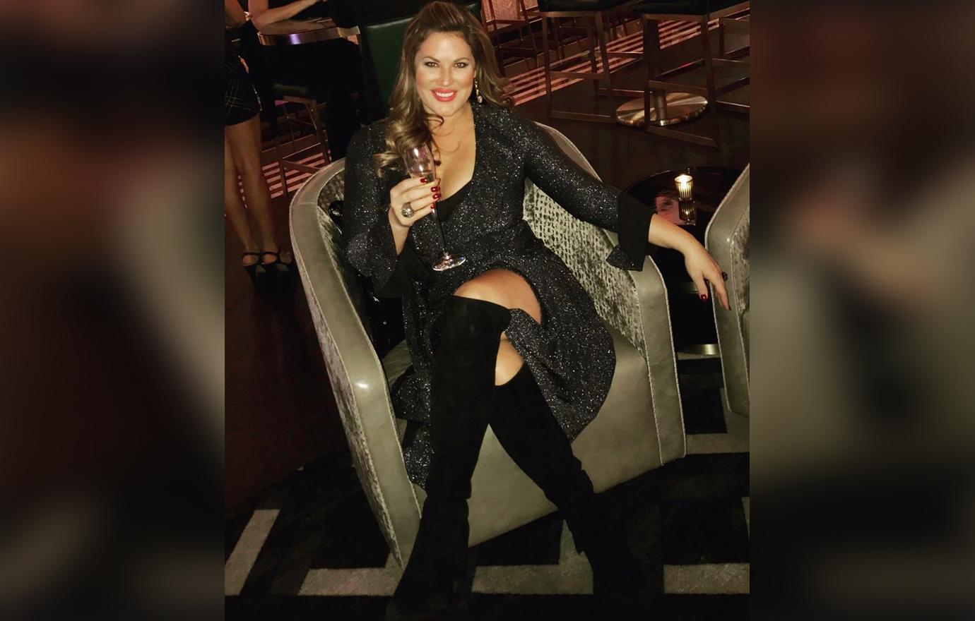 Emily Simpson Sitting Inside Lounge Wearing Black Dress and Knee High Boots Drinking Champagne and Smiling