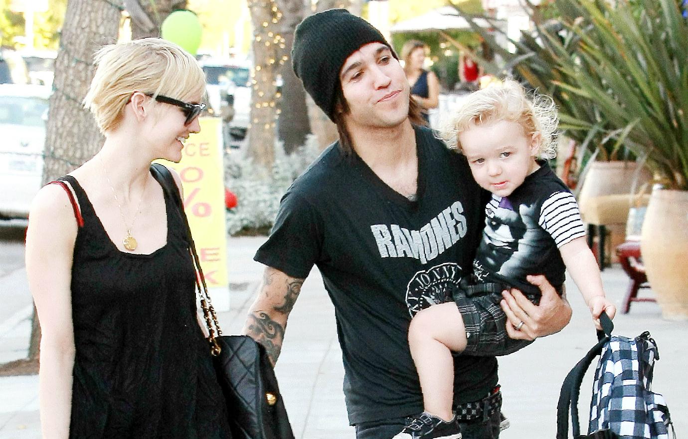 Ashlee Simpson in a black top and shades smiles at Pete Wentz, who wears a black hat and black Ramones t-shirt and holds their son Bronx.