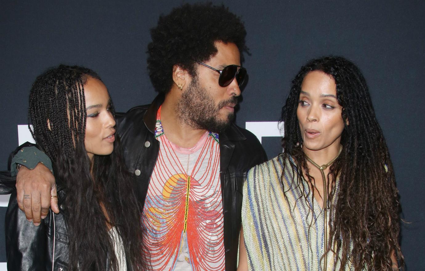 Lenny Kravitz, in a patterned tshirt, has his hands around daughter Zoe Bonet who wears a white dress and black leather jacket, and Zoe Bonet who wears a striped white dress.