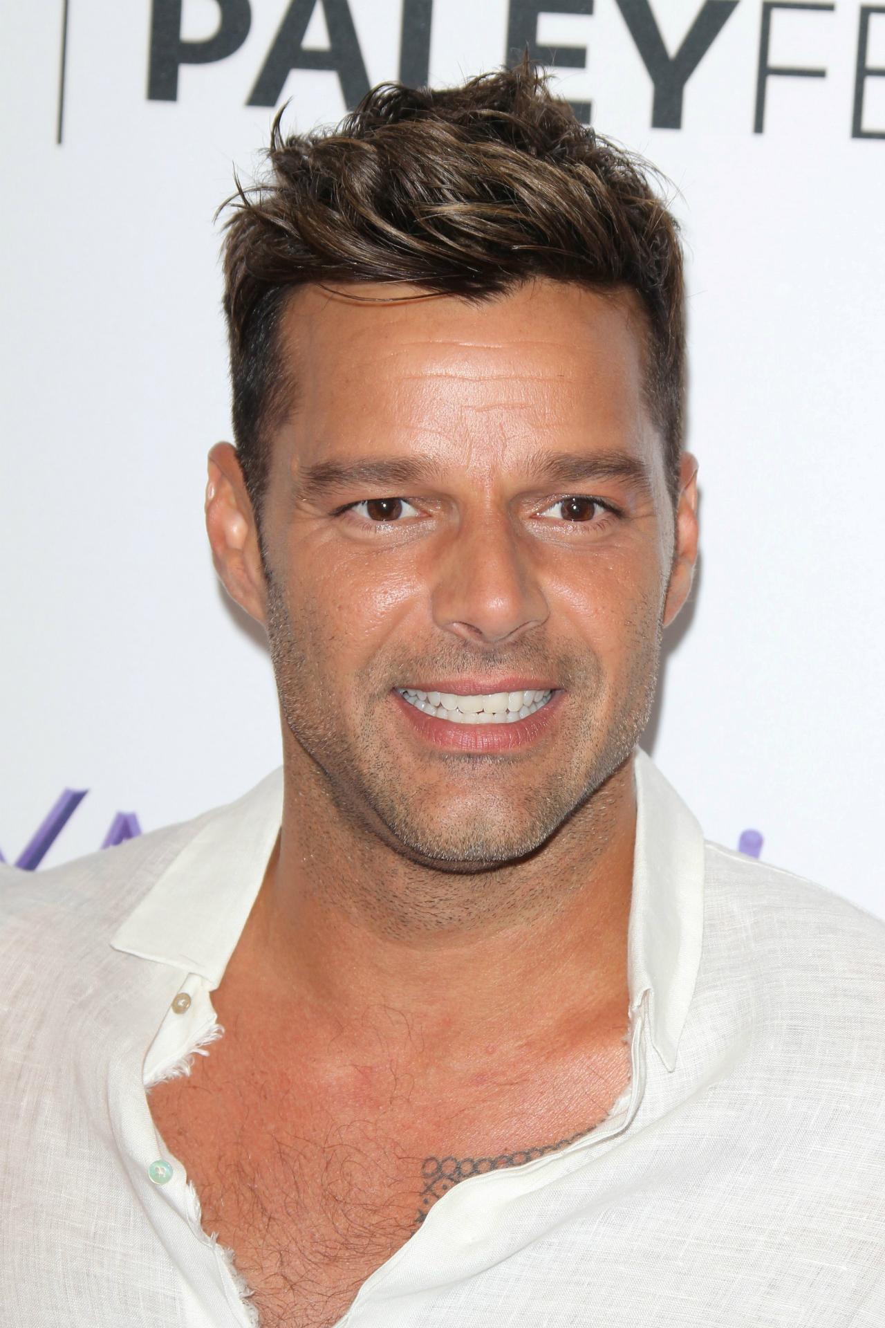 Ricky Martin wears a white unbuttoned shirt that shows off his chest hair.