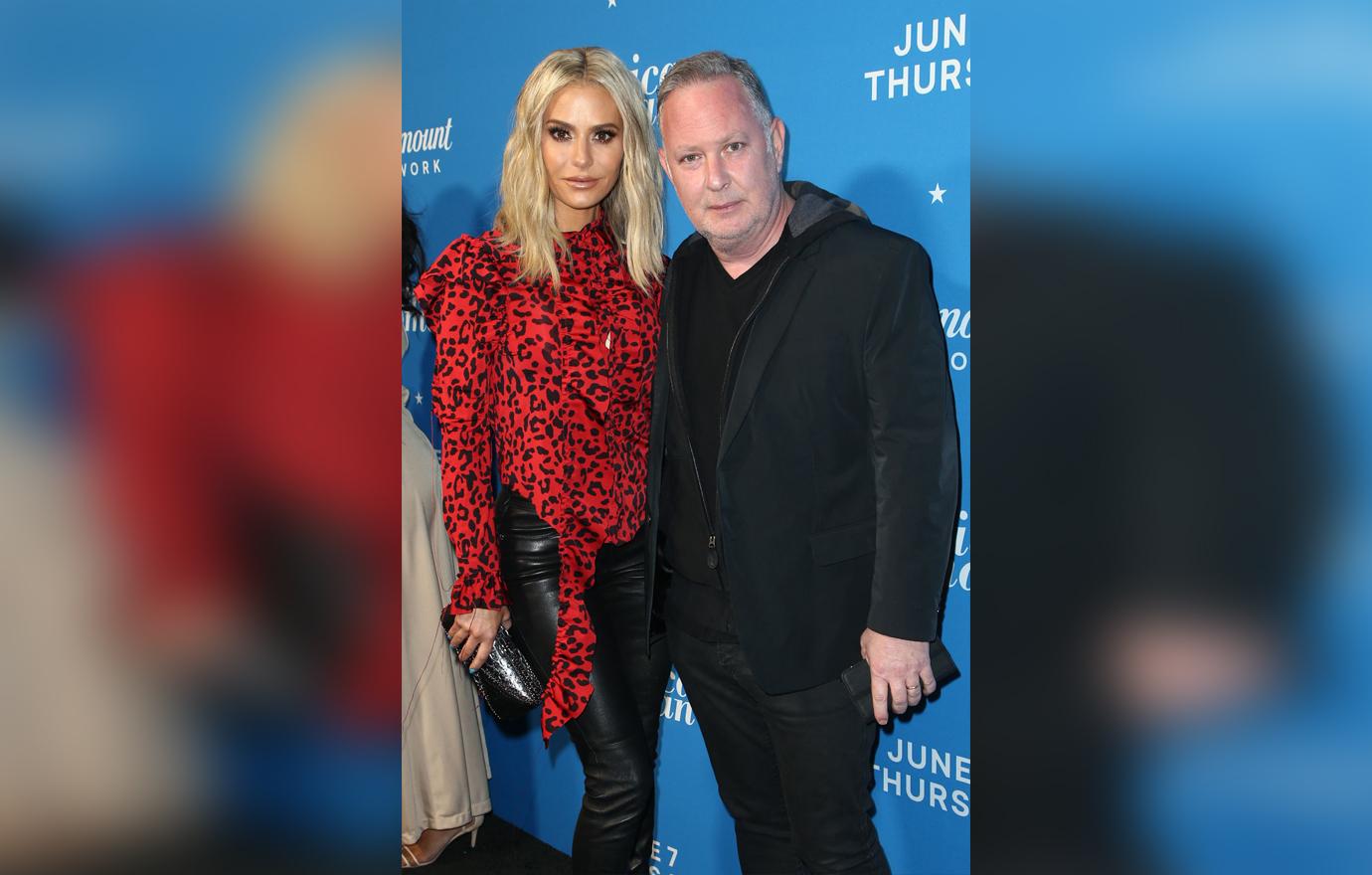 Paul Kemsley In A Black Suit and Dorit Kemsley in a Bright Red Ruched Leopard Print Top Pose Looking Serious on The Red Carpet