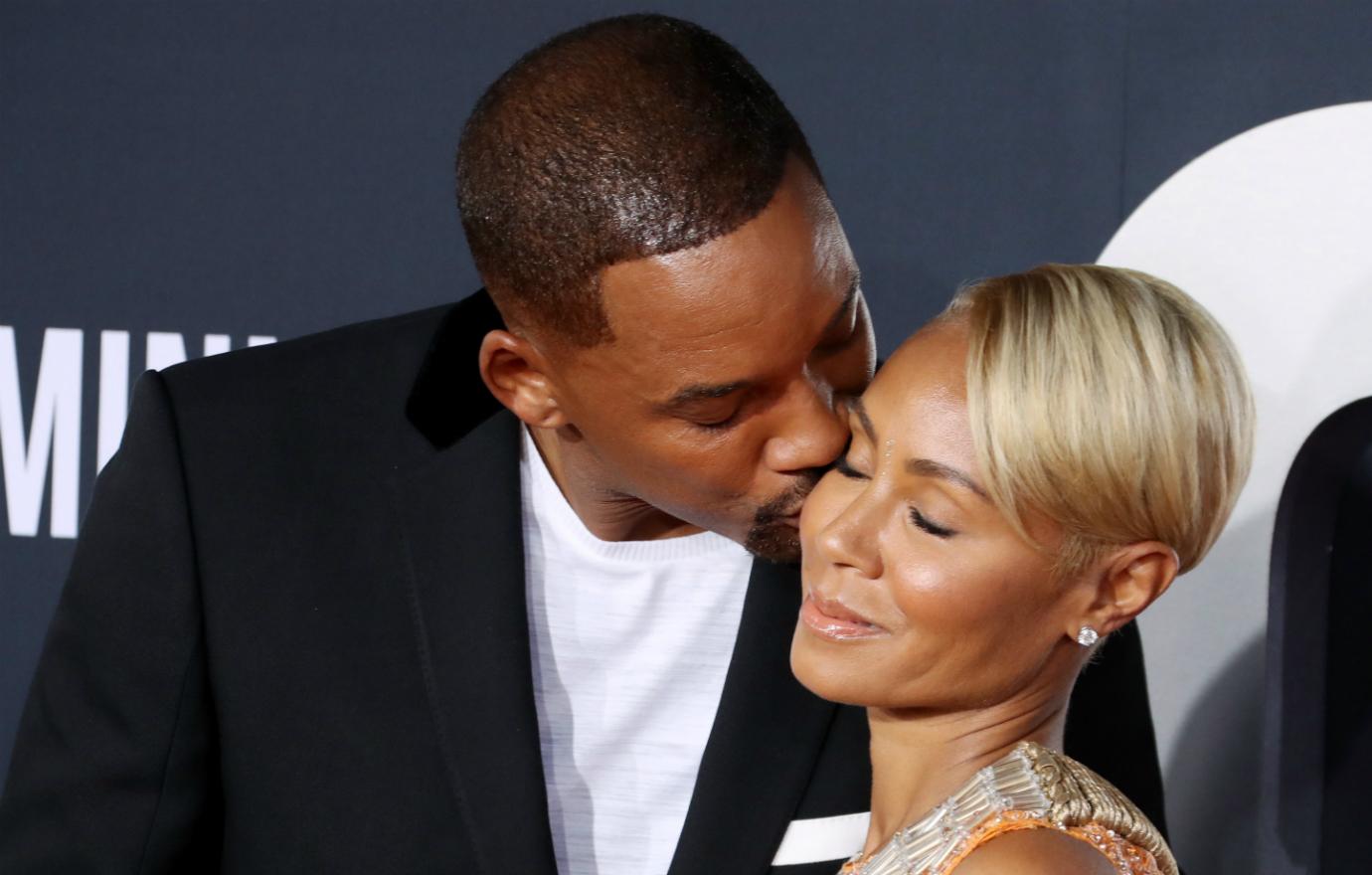 Will Smith kisses wife Jada Pinkett Smith on her cheek as they pose on the red carpet.