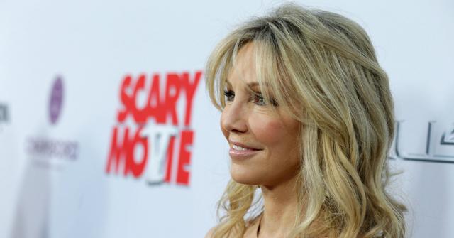 Heather Locklear, in a golden dress, stands on the red carpet and smiles.