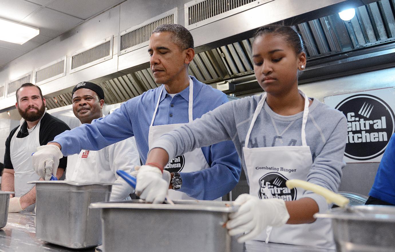 Sasha and Barack Obama volunteer in a kitchen