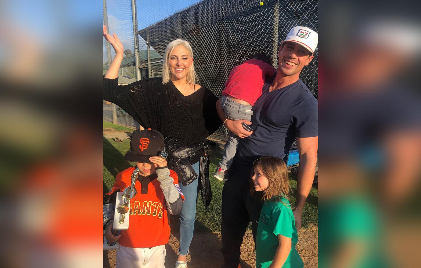 Gina Kirschenheiter and Matt Kirschenheiter Smiling at Baseball Field Where Son Wears Baseball Uniform and Holds a Trophy with Their Other Two Children