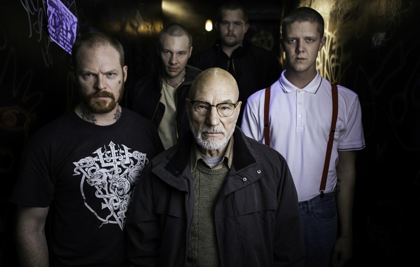 Patrick Stewart wore a brown collared shirt under a green sweater and a black jacket as he stood with his fellow onscreen Nazis in a photo from Green Room.