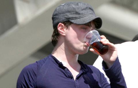 Daniel Radcliffe had a drink while watching an English cricket match in a long-sleeved, buttoned shirt.