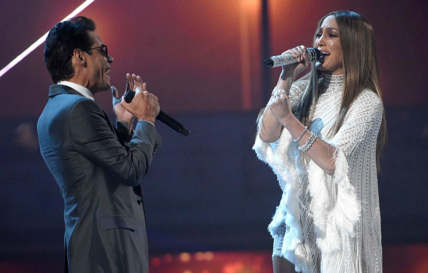 Marc Anthony, in a blue suit, sings with Jennifer Lopez who wears a white dress.