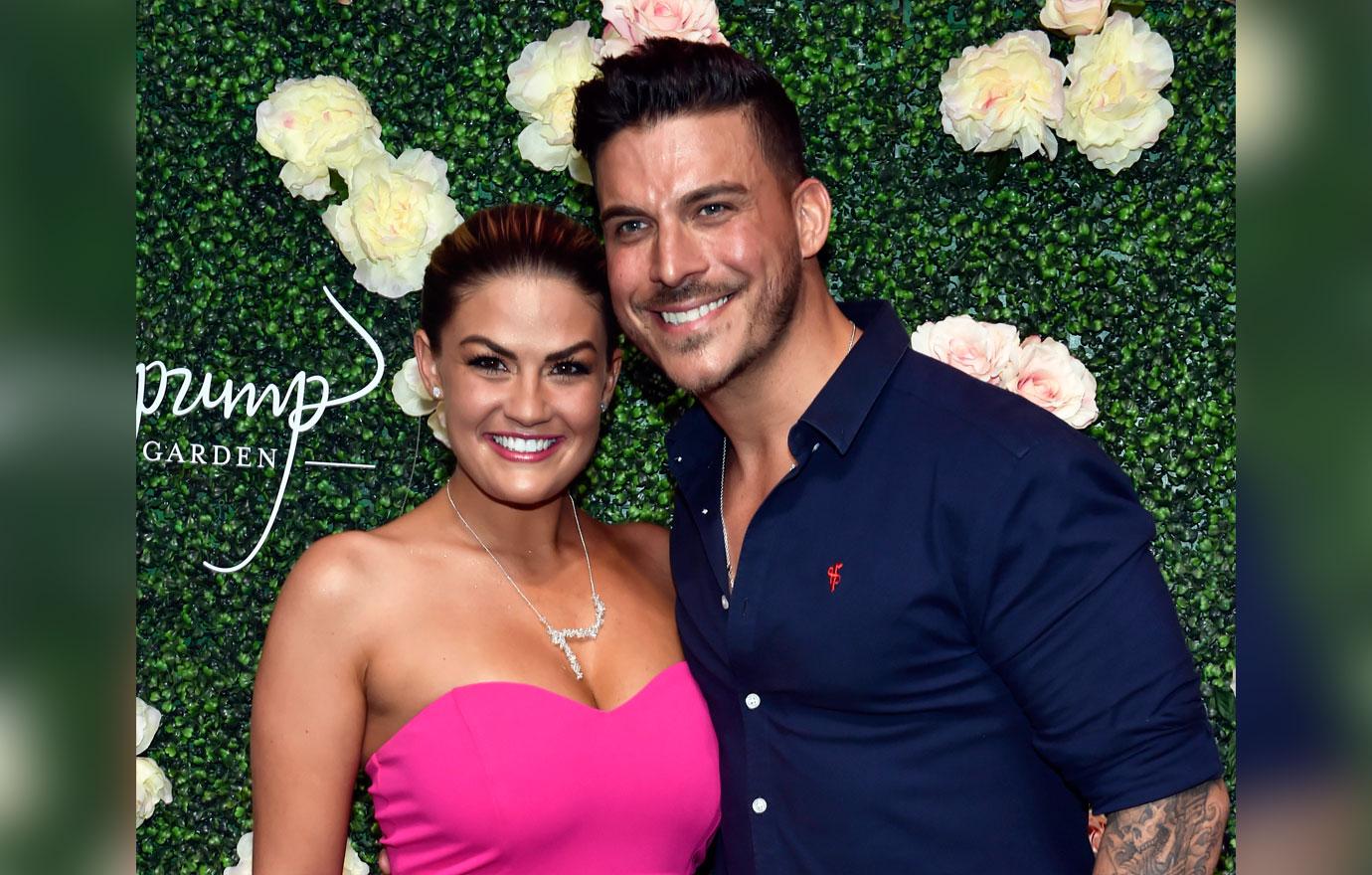 Brittany Cartwright Wearing Bright Pink Jumpsuit And Jax Taylor Wearing Navy Shirt Standing In Front of Flower Wall