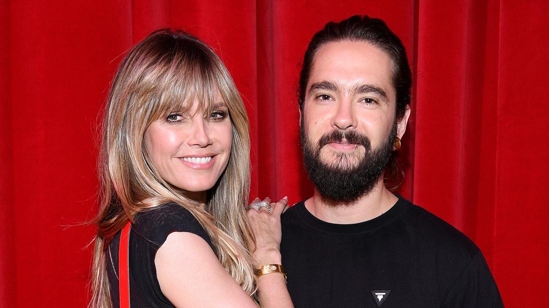 Heidi Klum Tom Kaulitz Smiling And Embracing In Front Of A Red Curtain