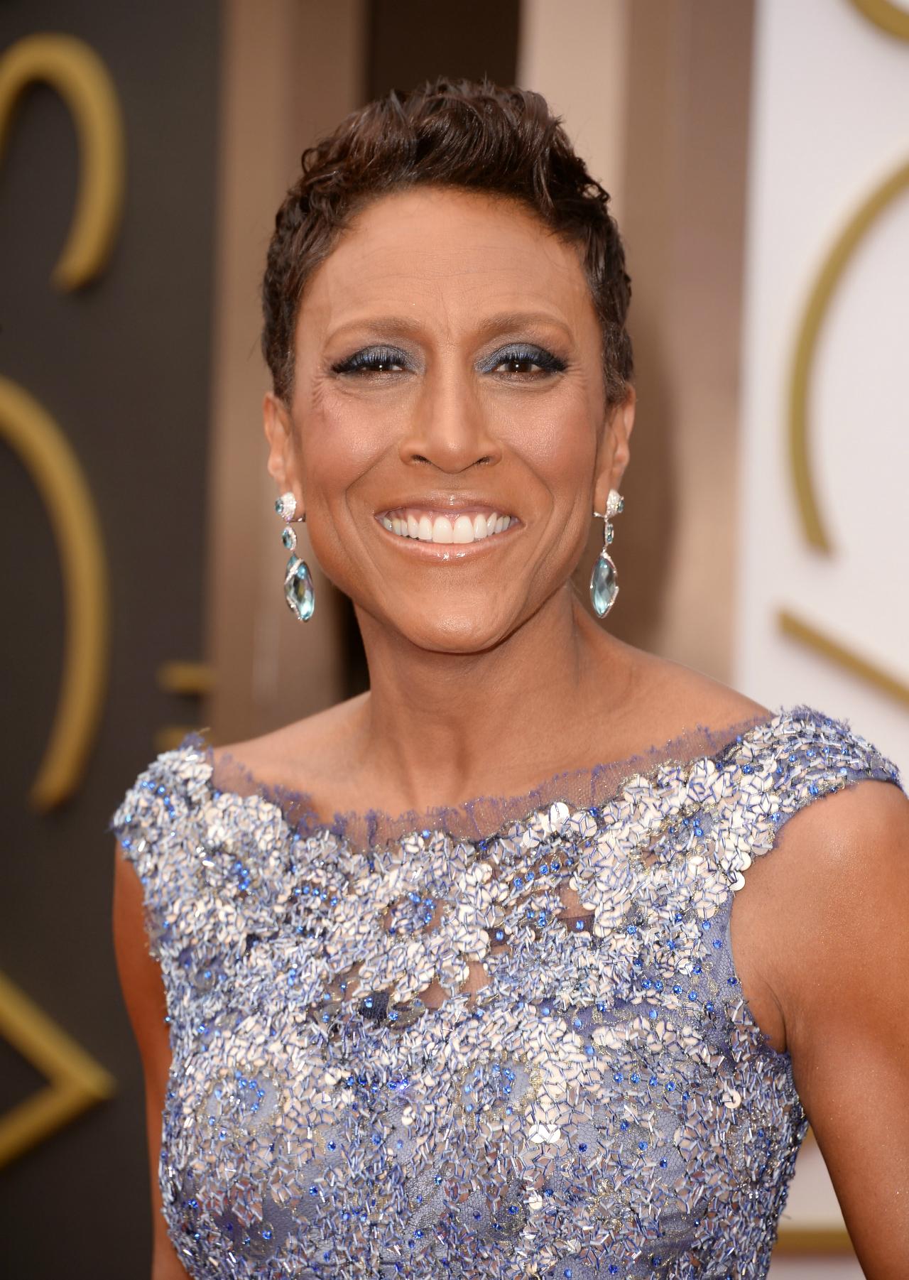 Robin Roberts wears a silver and blue beaded gown with large blue gemstone earrings and short hairstyle.