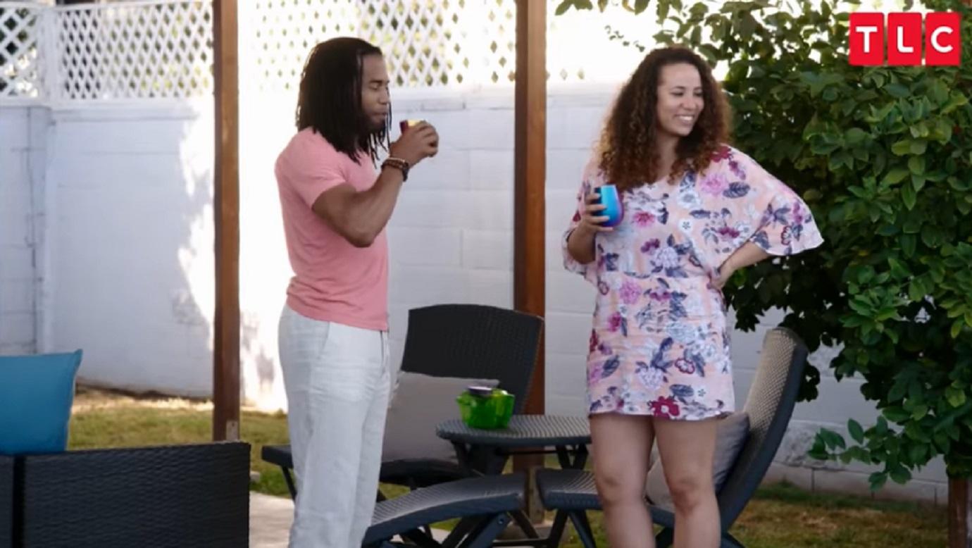 Dimitri Snowden stands next to Adrienne Cobb holding a drink while they talk.