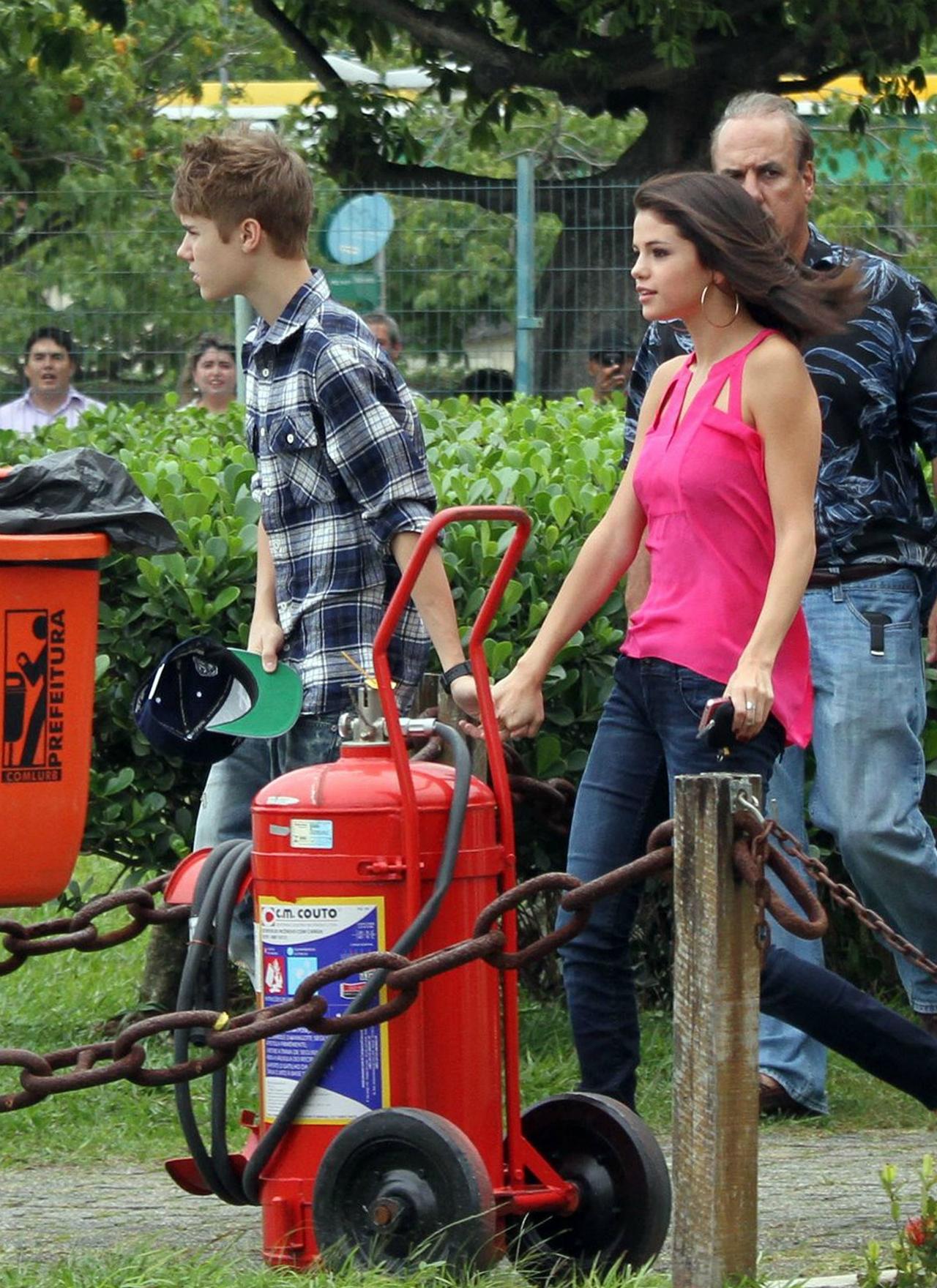 Selena Gomez wears a pink sleeveless top and jeans, holding hands with Justin Bieber wearing a flannel in jeans in 2011.