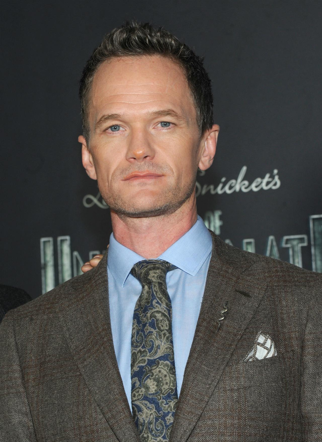 Neil Patrick Harris wears a gray suit, light blue shirt, and paisley blue tie.