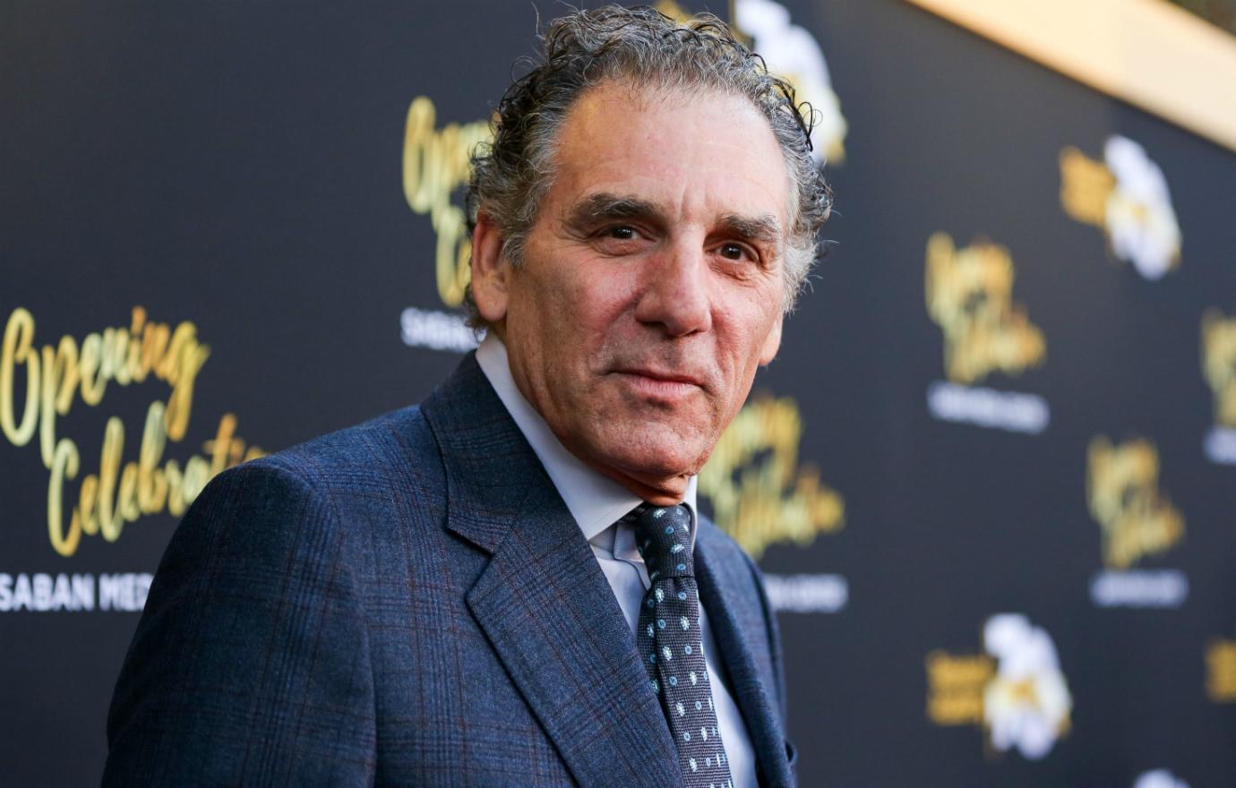 Michael Richards stands on the red carpet in a blue suit and patterned tie.