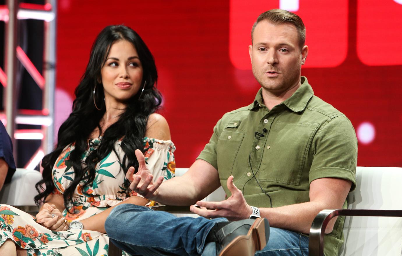 Paola Mayfield sits in a studio next to husband Russ Mayfield who wears a green top and blue jeans.