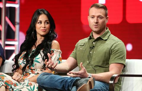 Paola Mayfield sits in a studio next to husband Russ Mayfield who wears a green top and blue jeans.