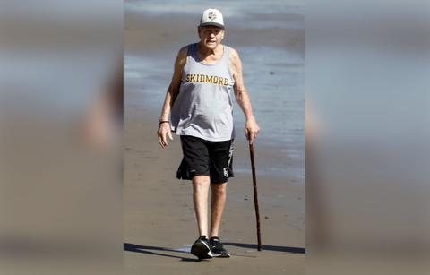 Ryan O'Neal Walking on Beach wWith a Cane Wearing Grey Tank and Black Shorts an Sneakers