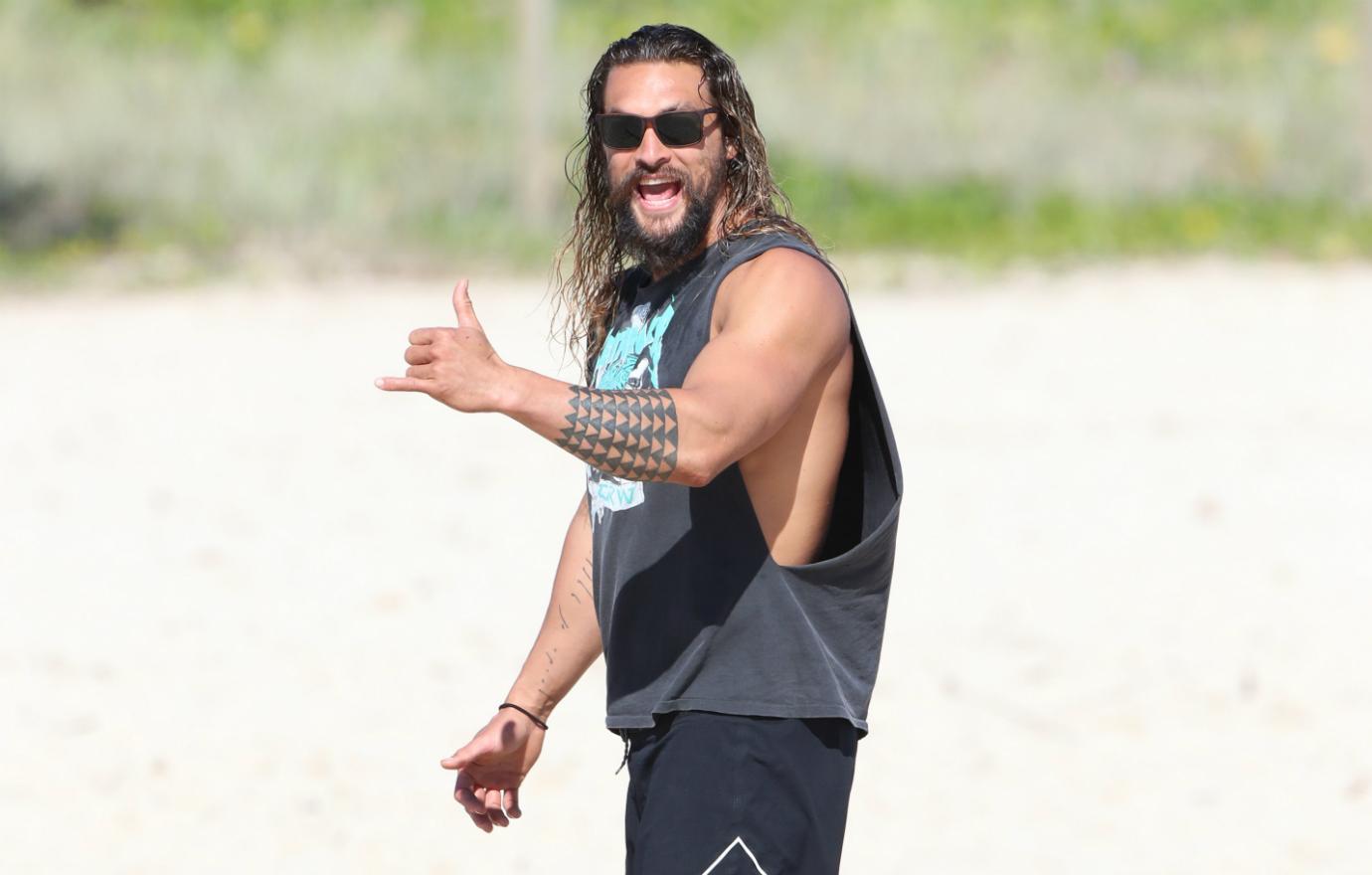 Jason Momoa has a little fun on a beach in Queensland, Australia while sporting classic board shorts and a torn open T-shirt.