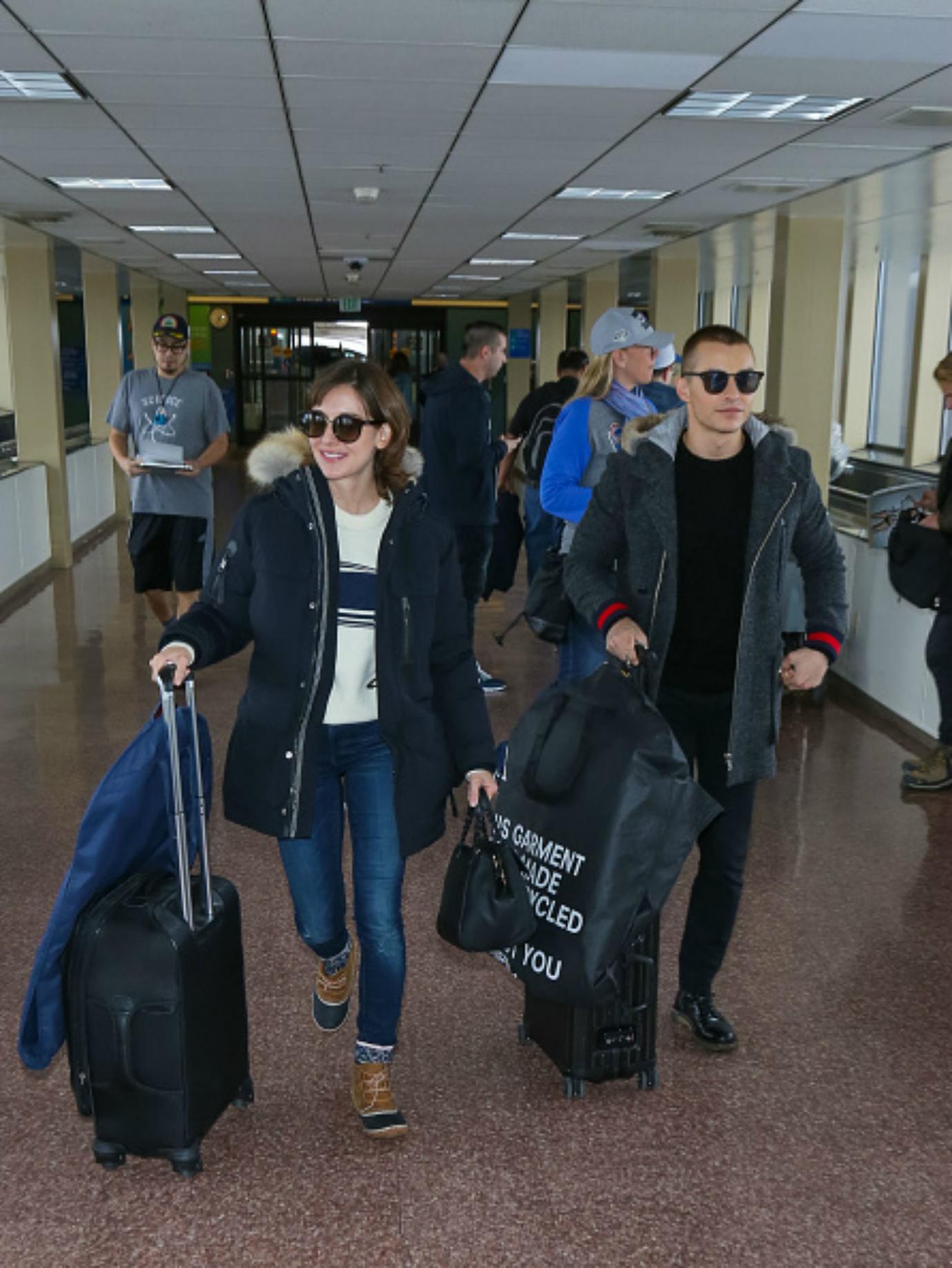 Alison Brie and Dave Franco walk carrying luggage.