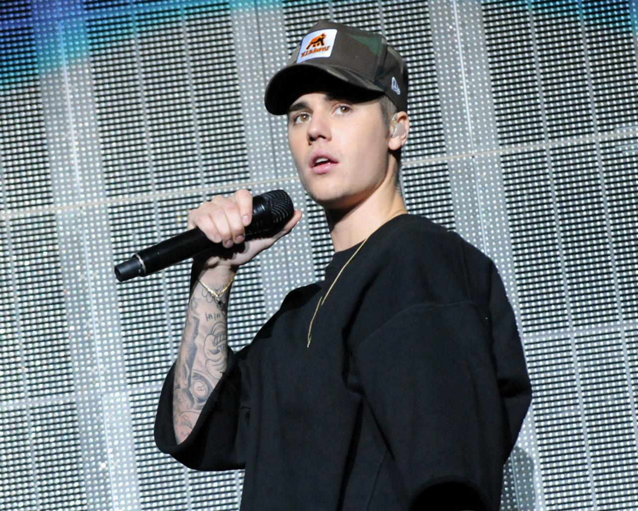 Justin Bieber wears a black sweatshirt and camo hat.