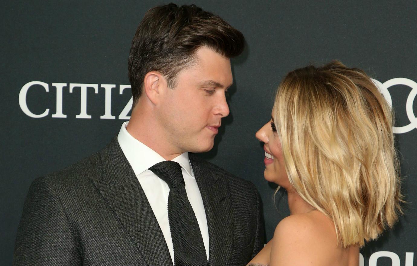 Colin Jost, in a black suit, gazes at Scarlett Johannson who smiles at him.